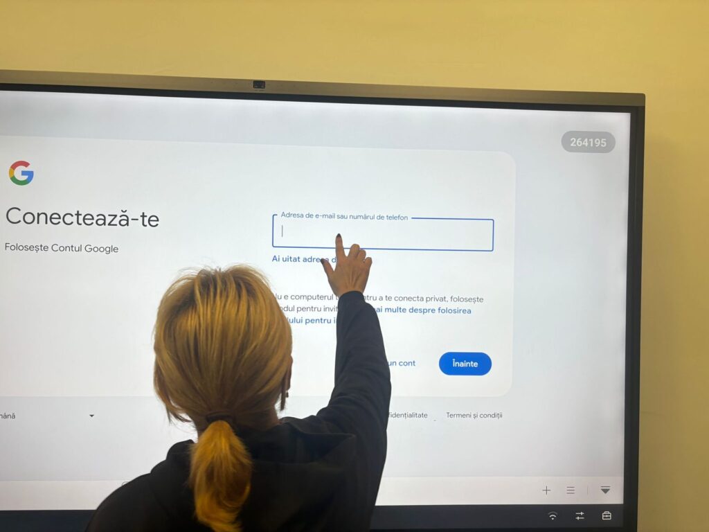 Persoană văzută din spate atingând un ecran interactiv pe care este afișată pagina de autentificare într-un cont de e-mail.