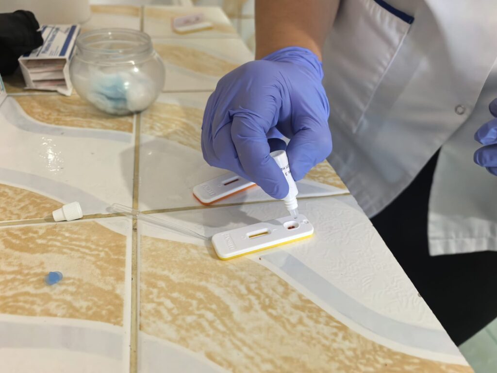 Mână în mănușă medicală aplicând soluția de test pe o casetă de testare rapidă, într-un cabinet de recoltare.